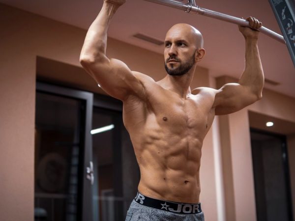 A bald, muscular man performing exercise on gym equipment indoors.