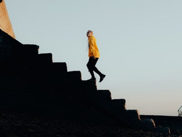 Stylish young man in vibrant streetwear walking up concrete stairs outdoors.