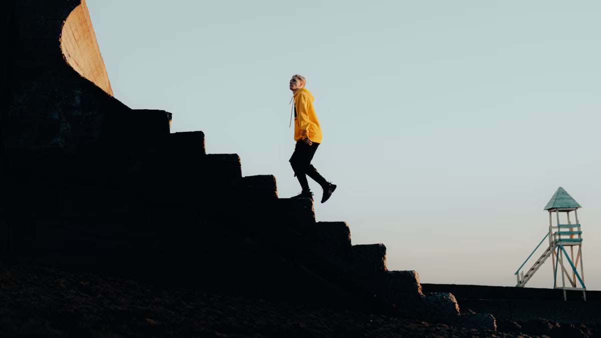 Stylish young man in vibrant streetwear walking up concrete stairs outdoors.